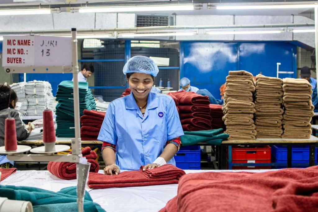 Smiling female factory worker organizes folded textiles in a busy production line.