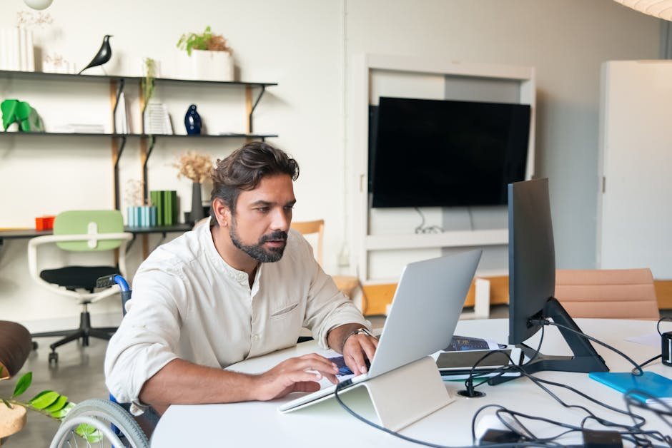 Professional man using a laptop in a modern office setting, showcasing accessibility and business environment.