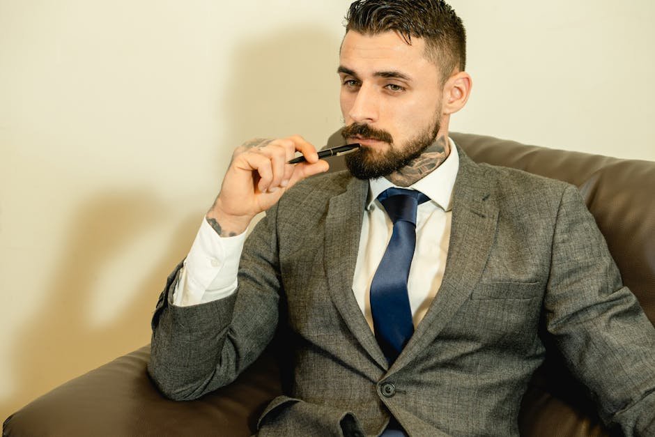 Thoughtful businessman with tattoos holding pen indoors. Professional and pensive look.